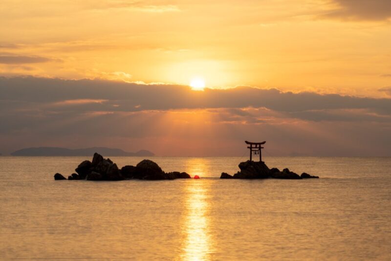 the sun overlooking the torii gate on a small island