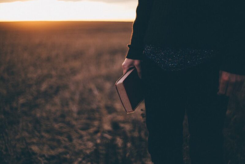 person standing in a field and holding a book
